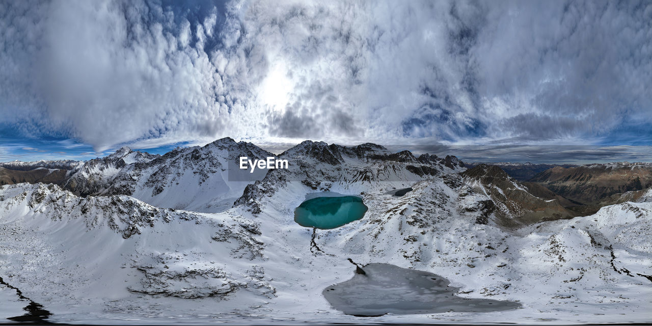 Panorama of mountain snow-covered range with turquoise lake, sunny day with clouds