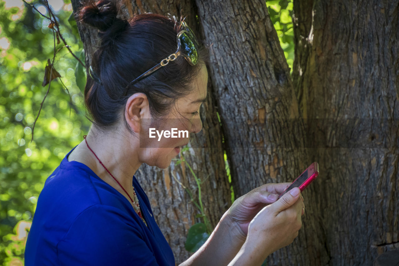 Side view of senior woman using smart phone by tree