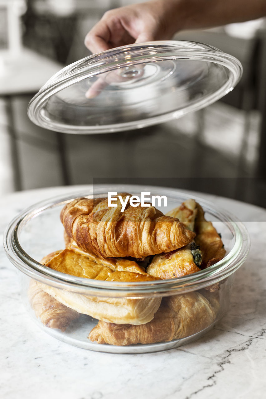 Cropped hand holding lid over container with croissants on table