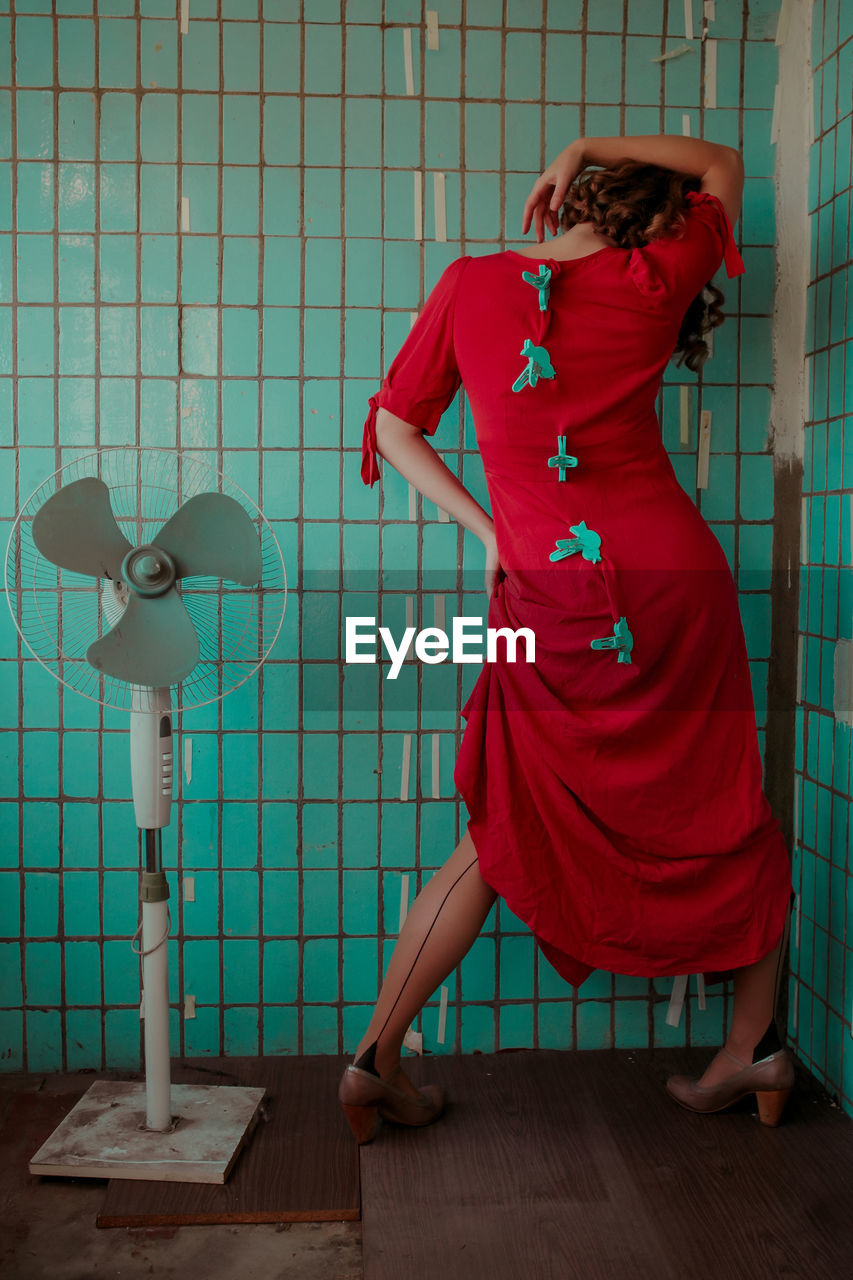 Rear view of woman in red dress with clothespins gesturing against wall