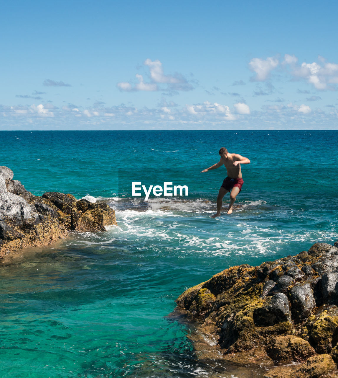 Low angle view of shirtless man jumping in sea from cliff against sky