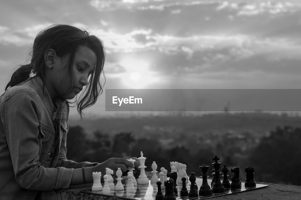 Portrait of young girl playing chess against cityscape 