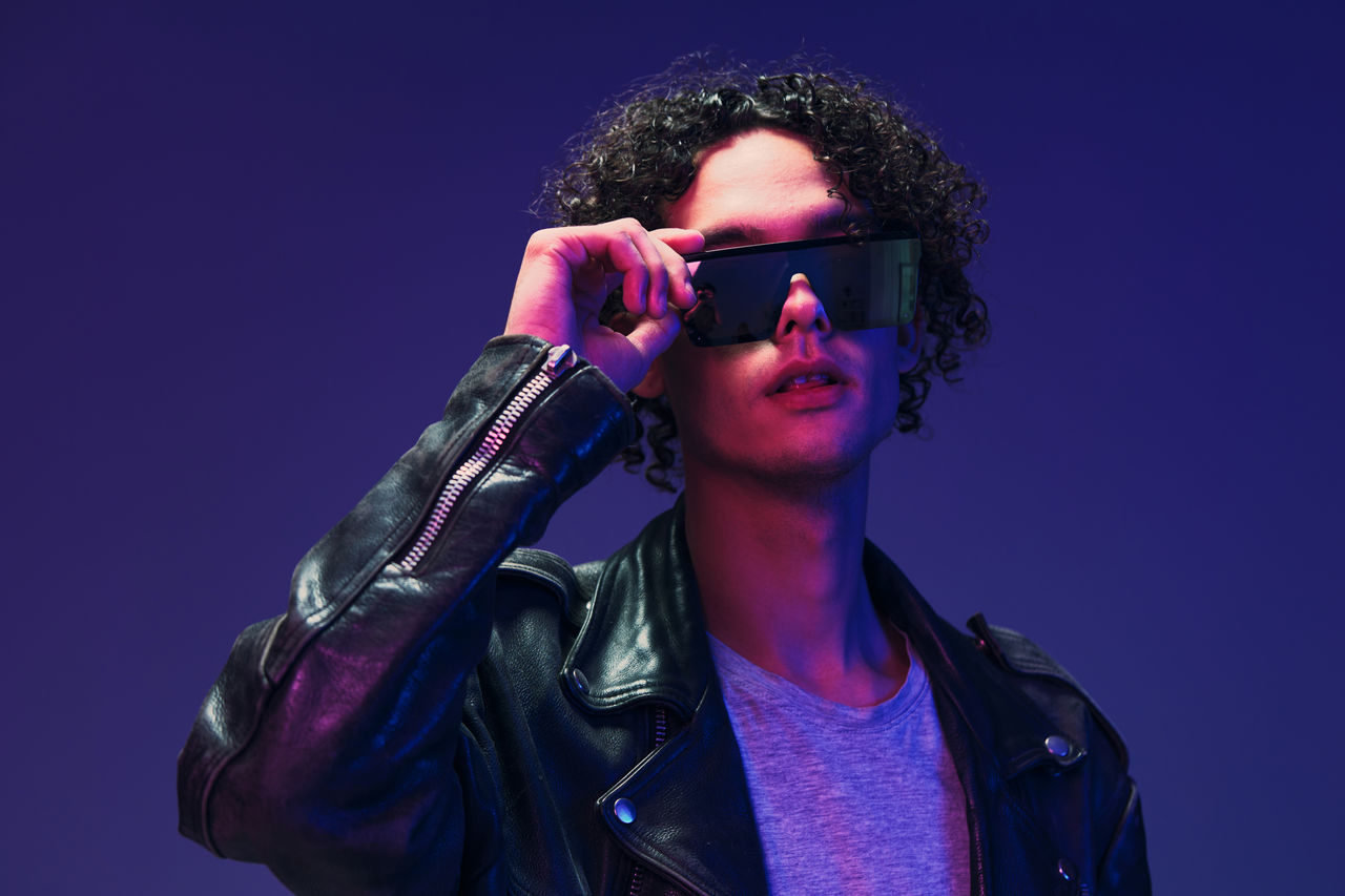 portrait of young man holding sunglasses against black background