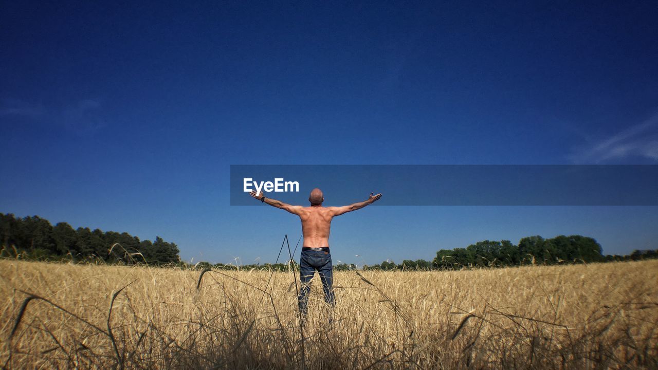 Rear view of shirtless man with arms outstretched standing on field