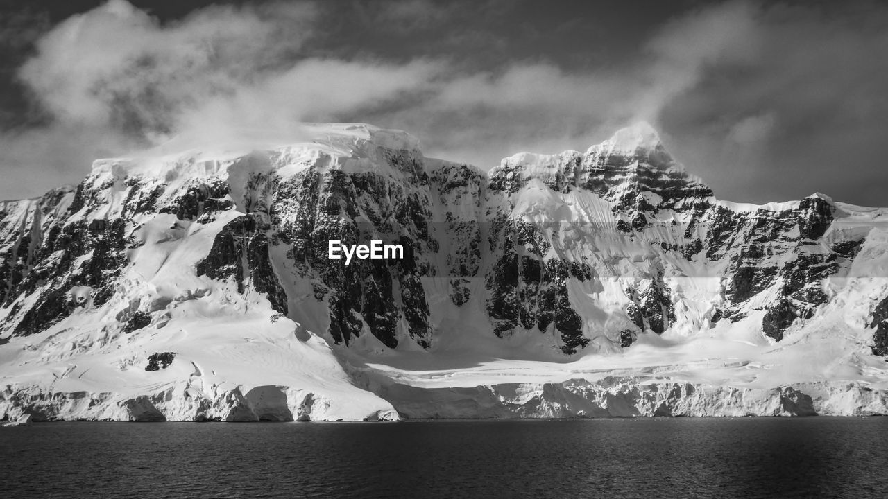 Black and white photo of glacier against snowcapped mountain in antarctica