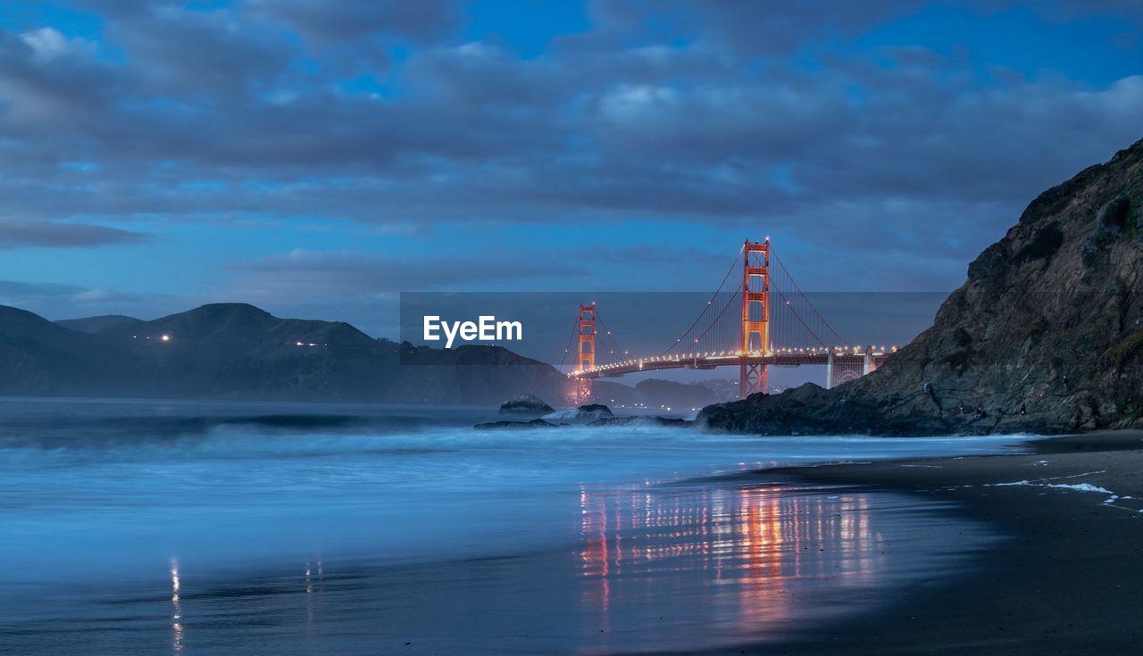 View of illuminated golden gate bridge over sea against cloudy sky at night