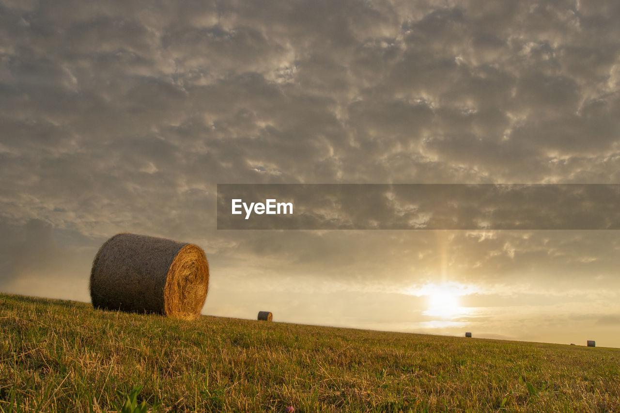 HAY BALES IN FIELD AGAINST SKY DURING SUNSET