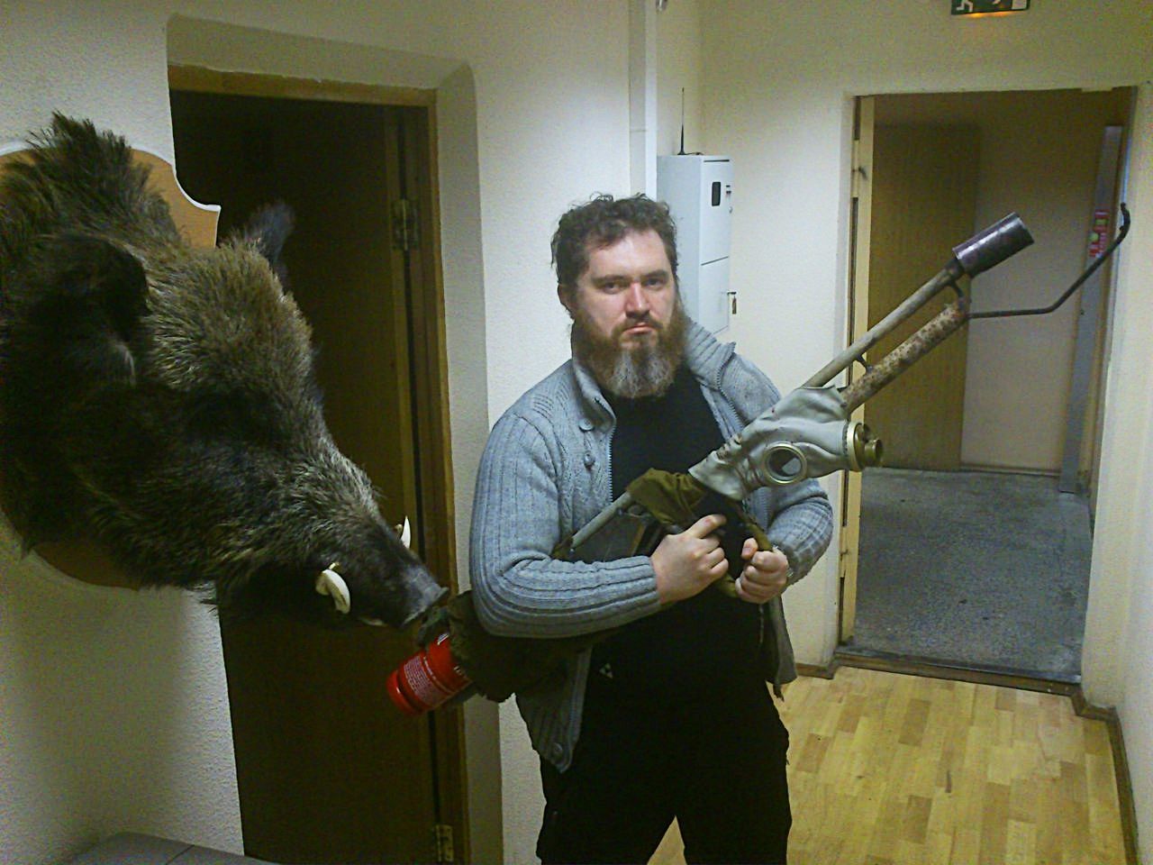 Portrait of man holding artificial gun by wild boar trophy at home