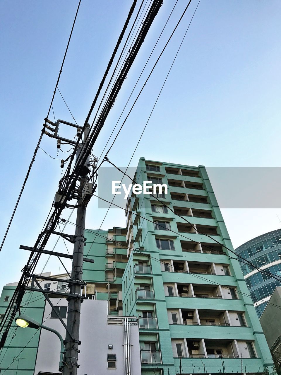 Low angle view of electricity pylon and building against clear sky