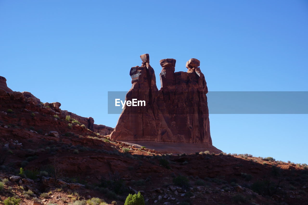 sky, rock, nature, rock formation, travel destinations, landscape, scenics - nature, travel, environment, clear sky, beauty in nature, land, mountain, blue, non-urban scene, arch, wilderness, outdoors, natural environment, day, geology, desert, tourism, formation, landmark, no people, full length, leisure activity, tranquility, terrain, low angle view, sunny, valley, tranquil scene