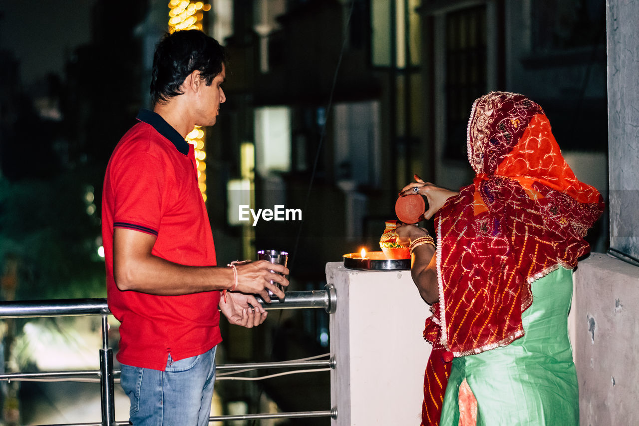 Woman standing with man on terrace during karva chauth at night