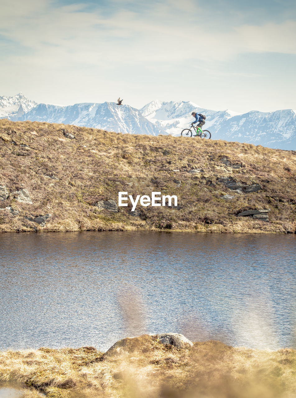 Side view of man riding bicycle on hill by lake