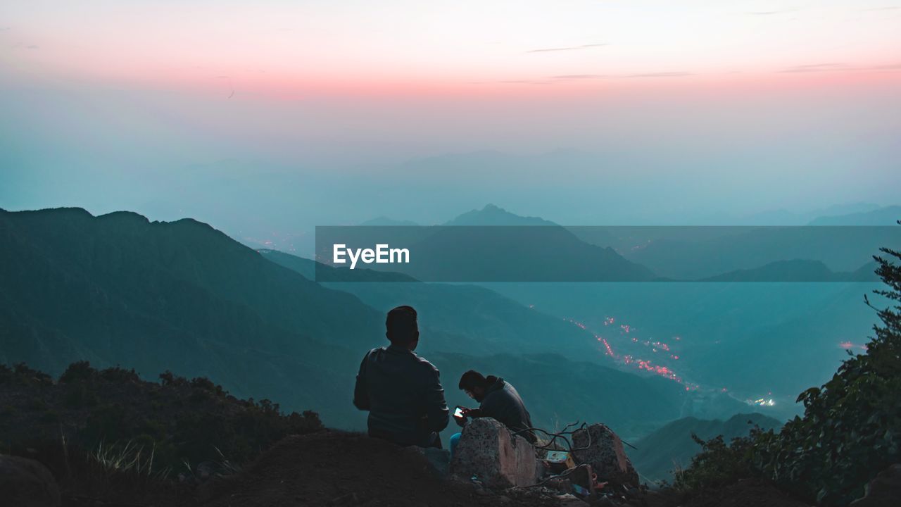 People sitting on mountain against sky during sunset