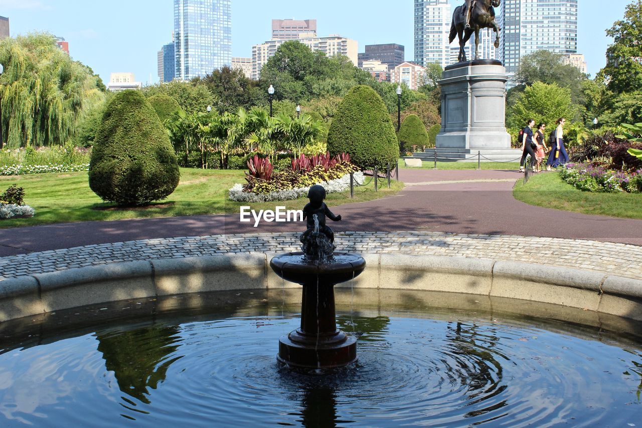 FOUNTAIN BY LAKE IN PARK AGAINST BUILDINGS