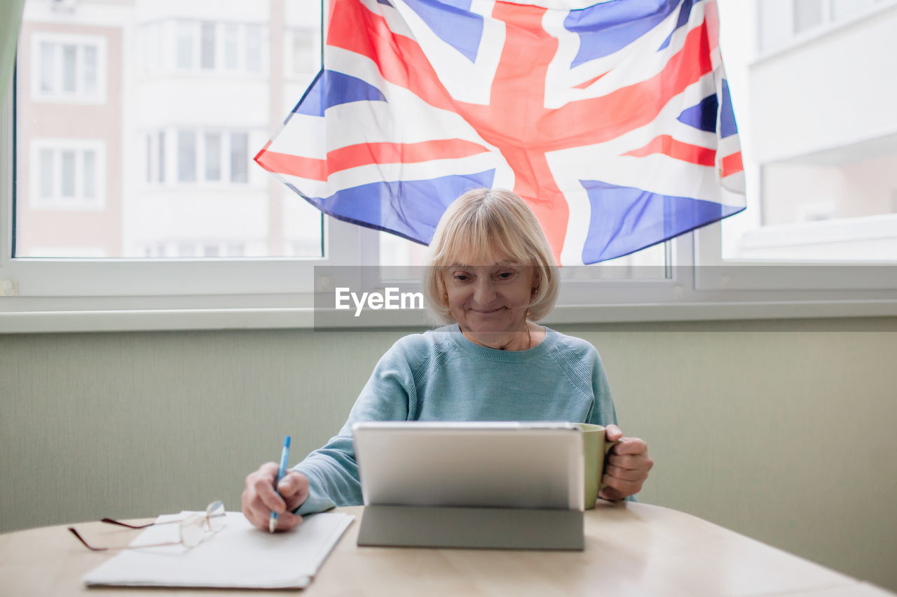 Senior woman learns english via internet with laptop, language classes for ukrainian refugee