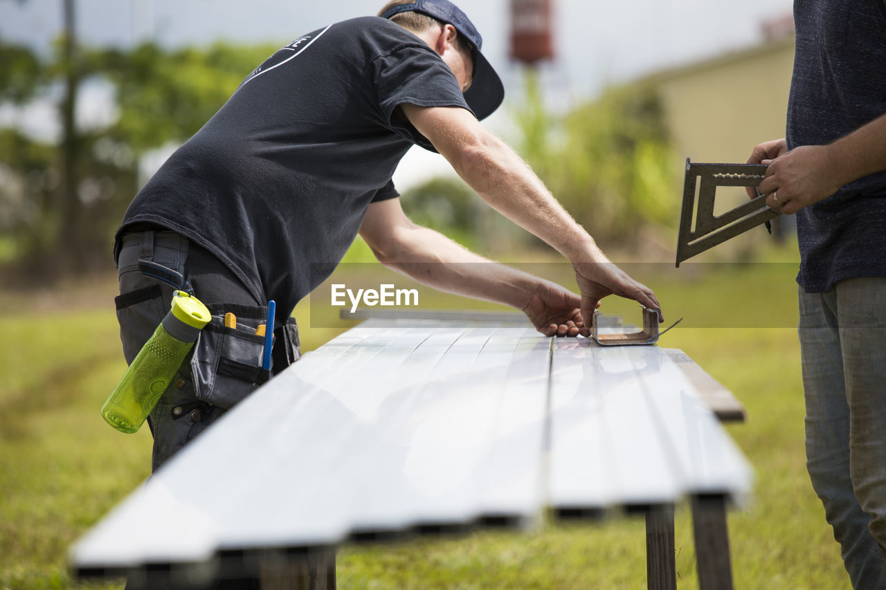 Two men measure brackets for mounting solar panels.