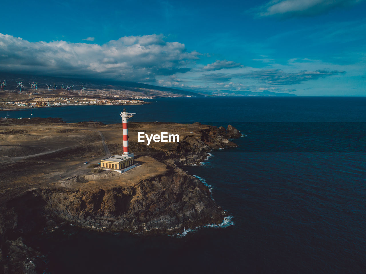 Lighthouse amidst sea and buildings against sky