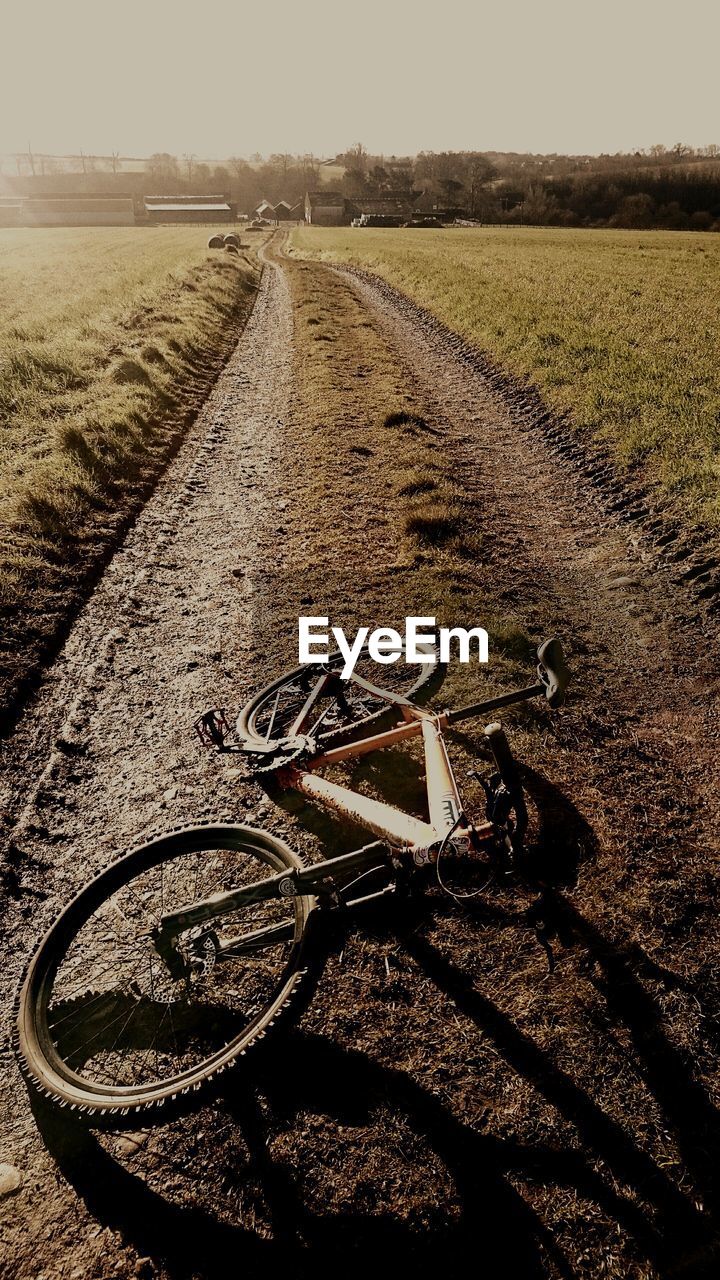 High angle view of fallen bicycle on dirt road amidst field during sunny day
