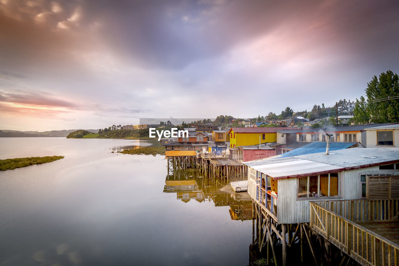 HOUSES BY LAKE AND BUILDINGS AGAINST SKY