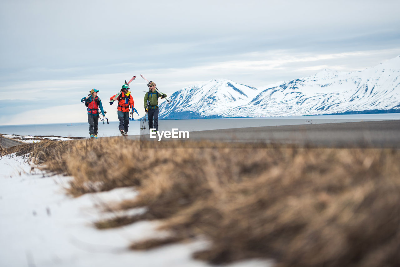 Three people walk along a paved road with mountains and ocean behind