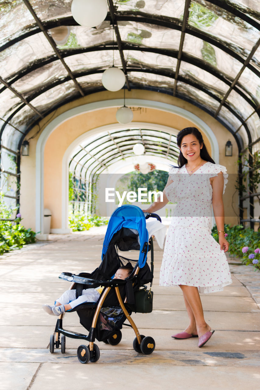 Portrait of smiling woman with son in baby stroller standing under archway