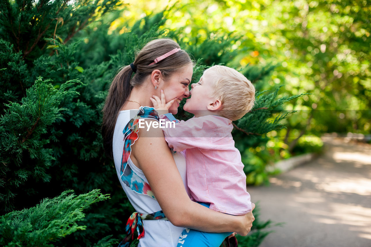 Happy mother and daughter standing against trees