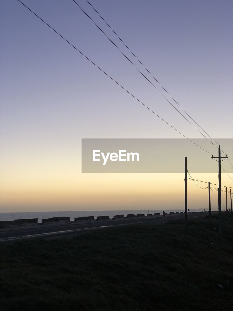 SILHOUETTE ELECTRICITY PYLONS ON LAND AGAINST SKY DURING SUNSET