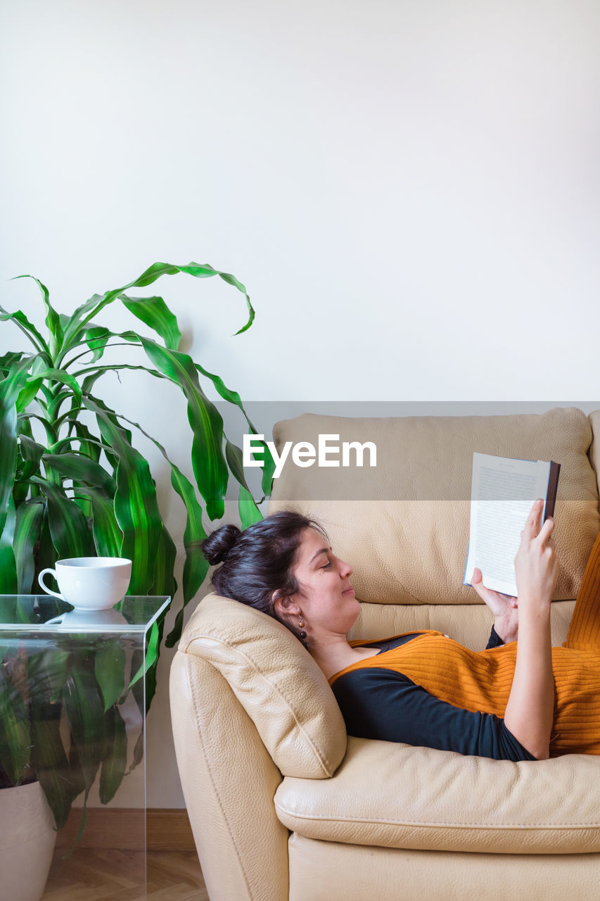 Woman reading book while sitting on sofa at home