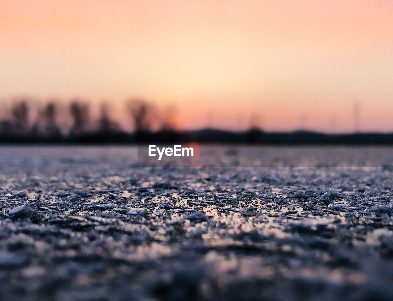 Surface level on lakeshore against orange sky during winter