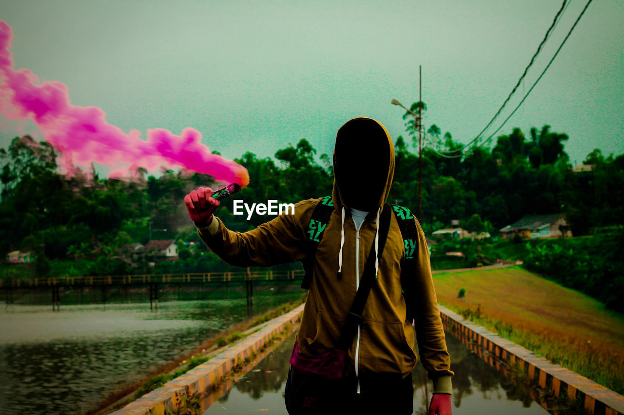 Man wearing hooded shirt while holding pink distress flare