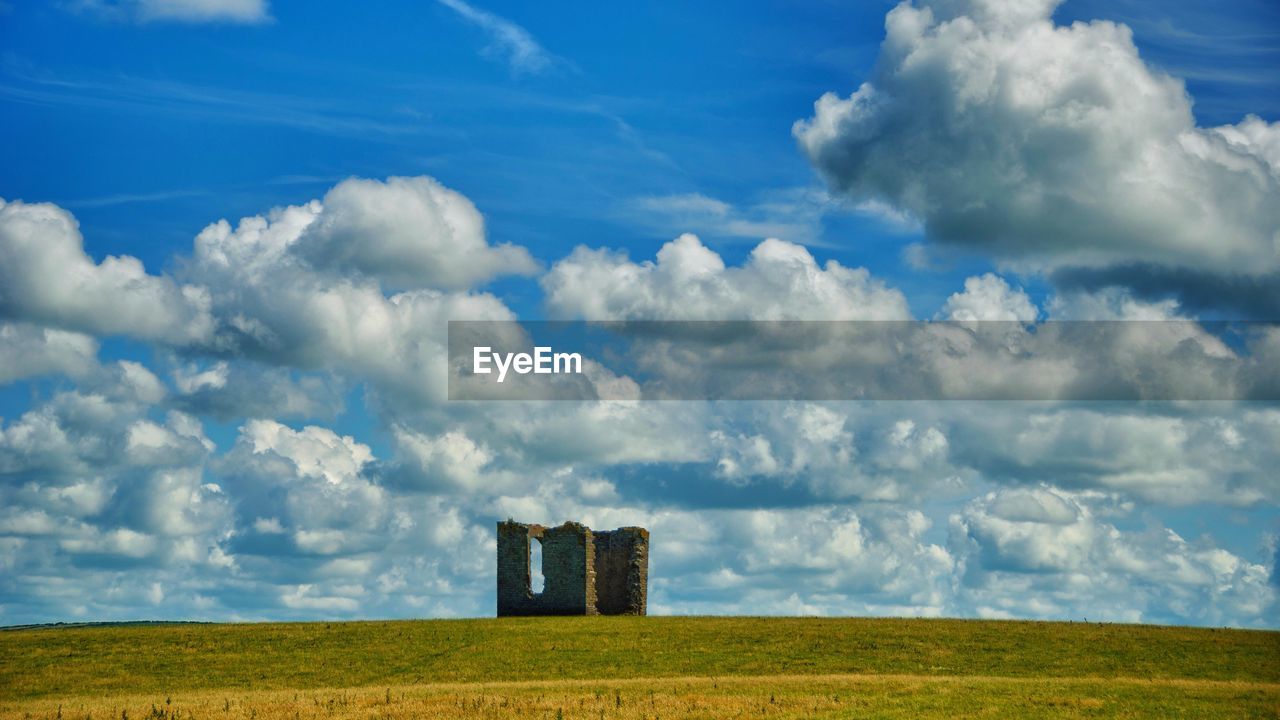Old ruin on grassy landscape against cloudy blue sky during sunny day