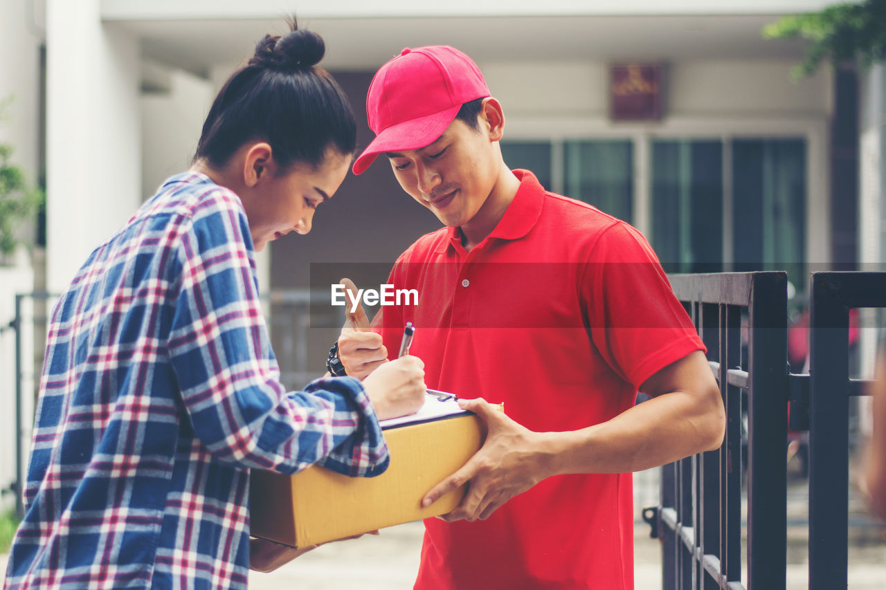 Female customer signing receipt while receiving package from delivery man at gate