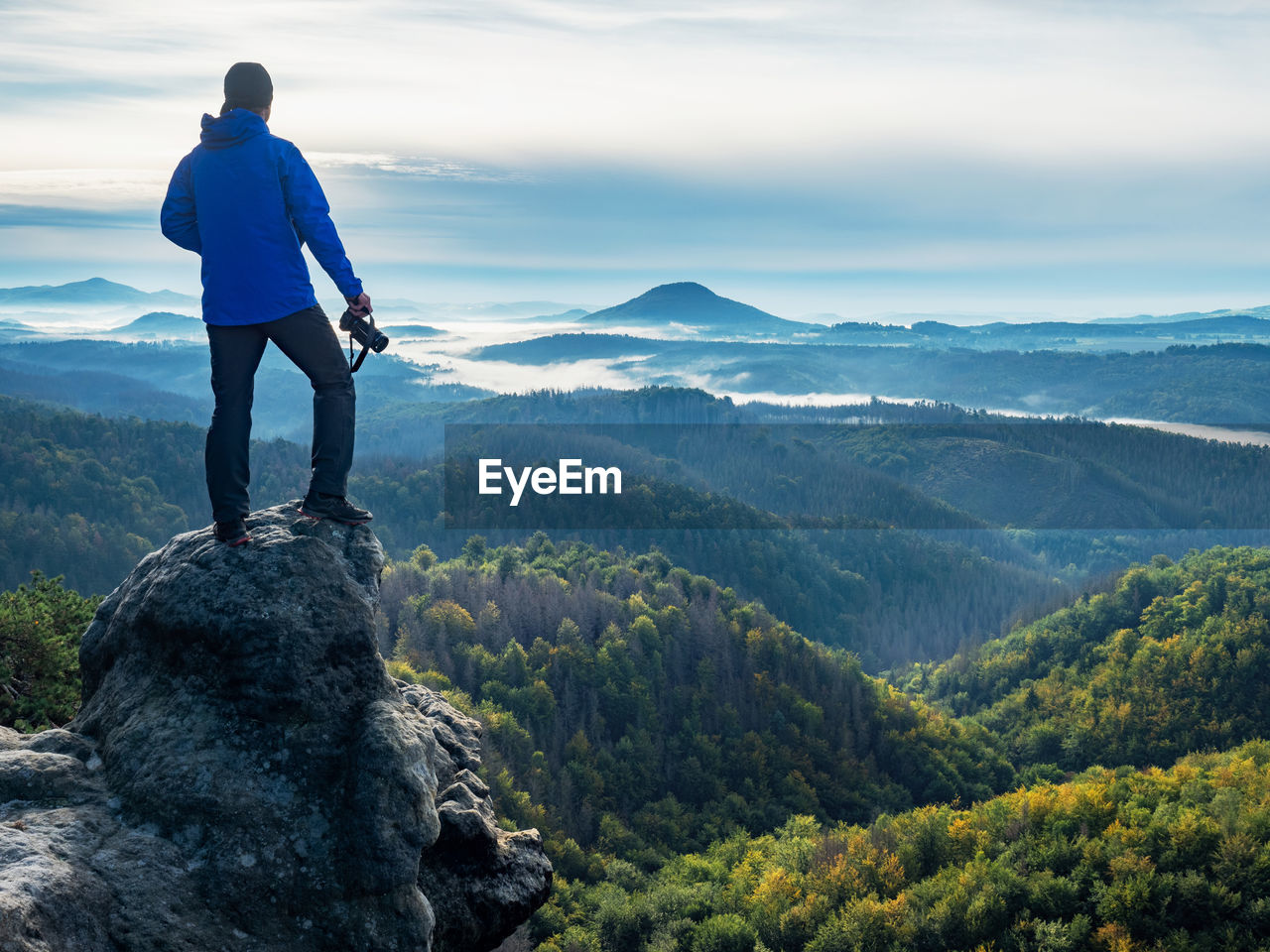 Camera in the hand of man standing on rock and looking into landscape. photographer and camera