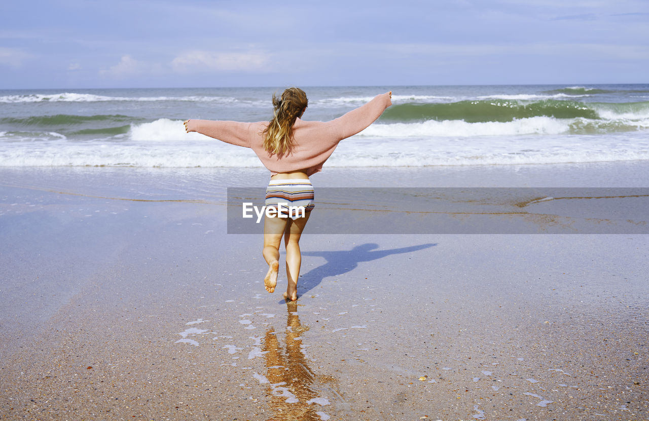 Teenage girl running on beach toward ocean