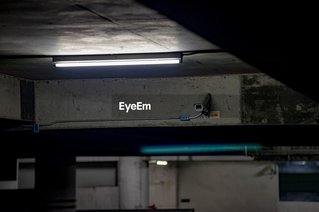 Security camera on illuminated ceiling at underground parking lot