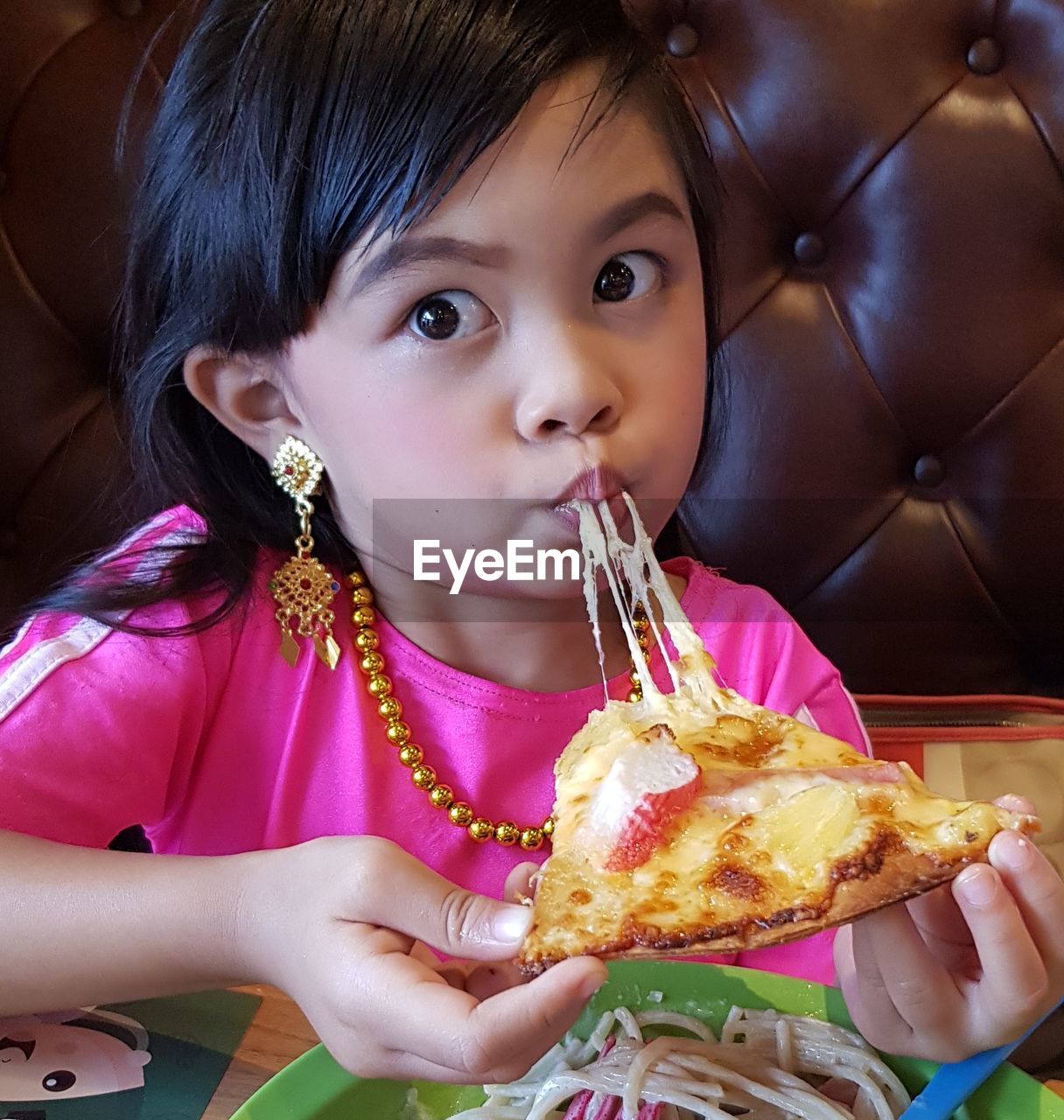 Cute girl eating pizza while sitting in restaurant