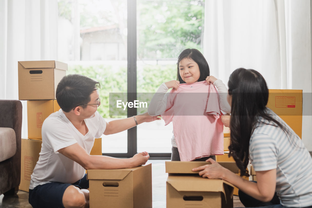 Smiling parents looking at daughter showing clothes in new house