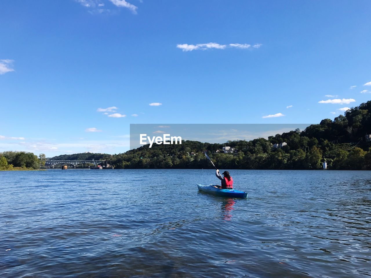 Woman kayaking on river against blue sky