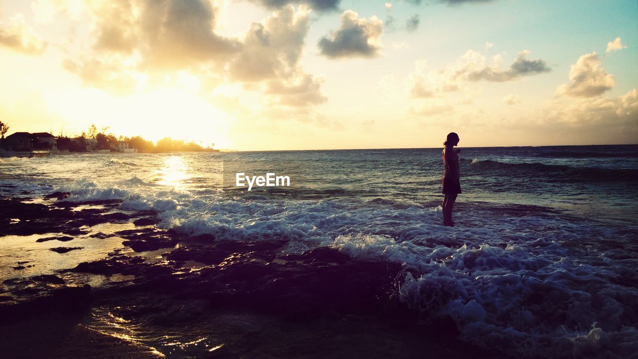 Silhouette woman standing on beach against sky during sunset