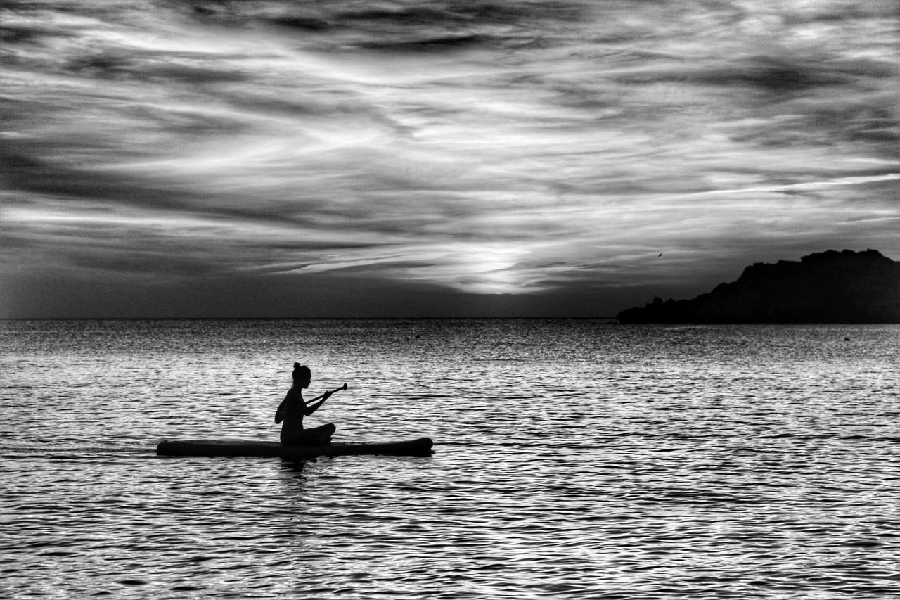 Silhouette woman in boat on sea against sky at dusk