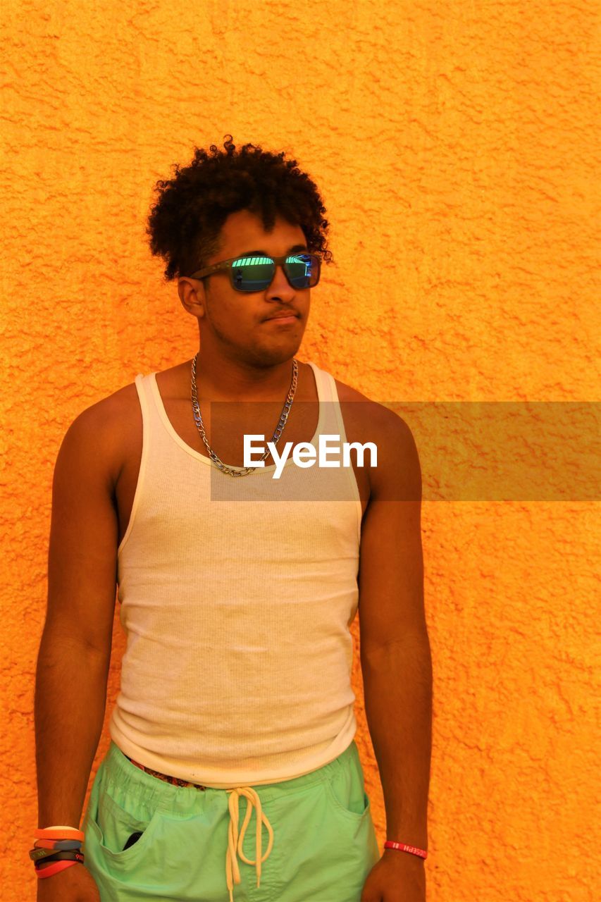 Teenage boy wearing sunglasses while standing against orange wall