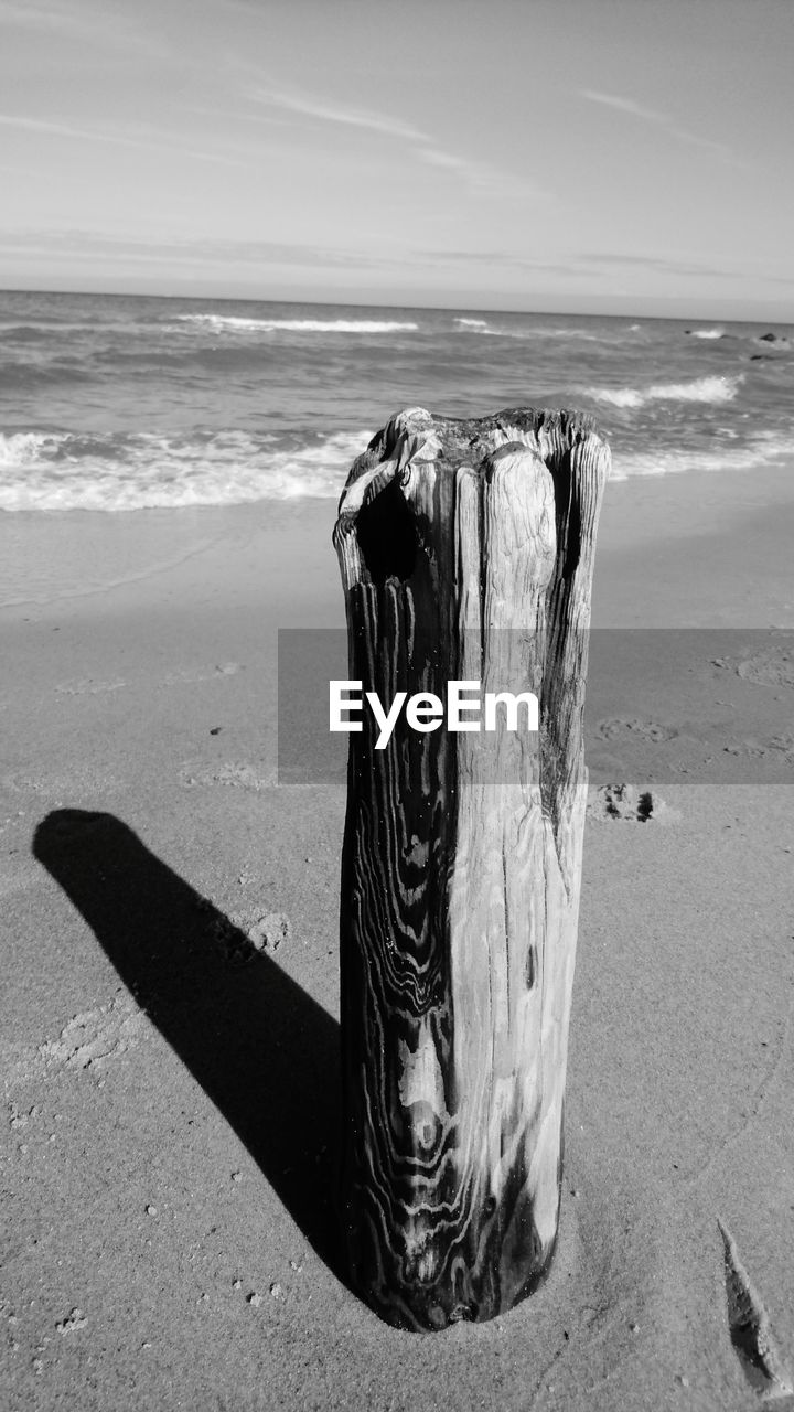 SHADOW OF WOODEN POST ON BEACH