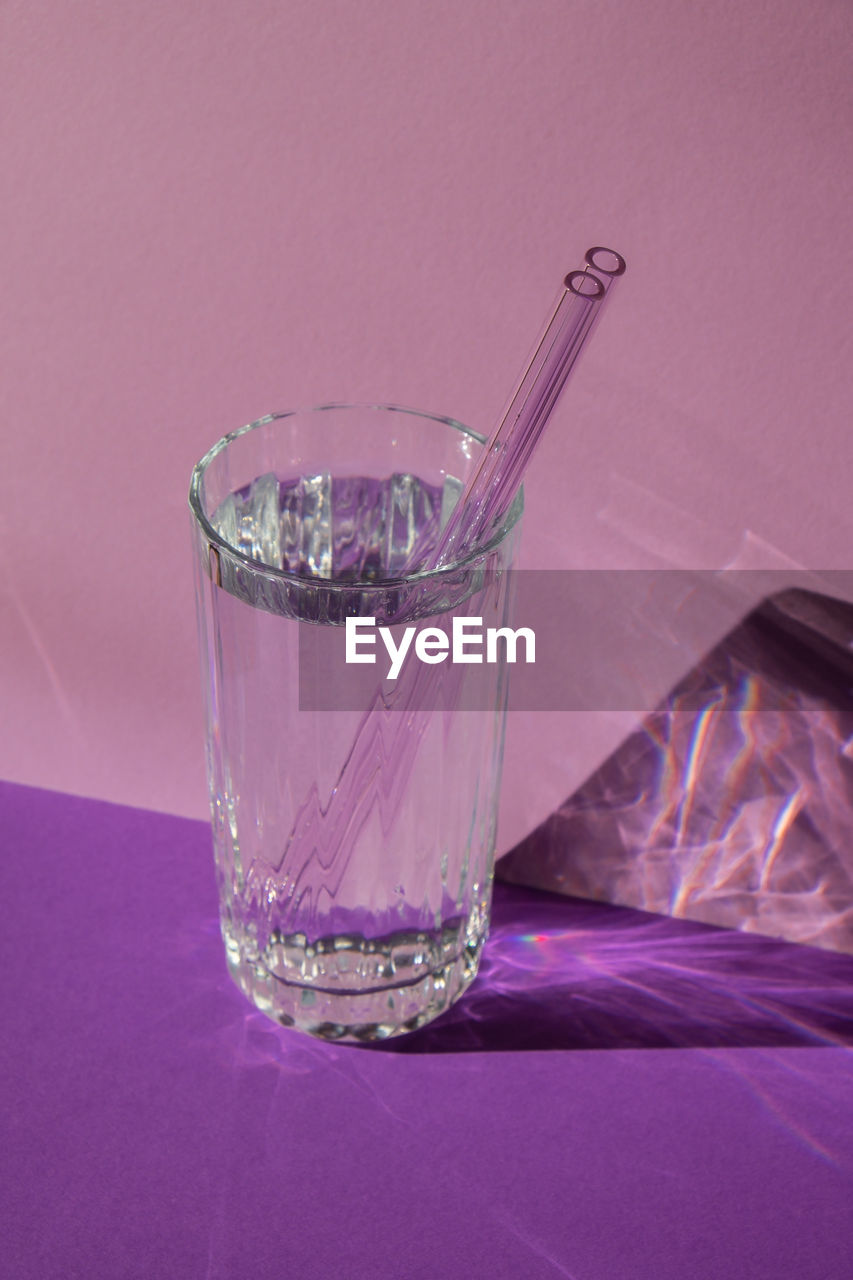 Reusable glass straws in glass with water on purple violet background eco-friendly drinking straw