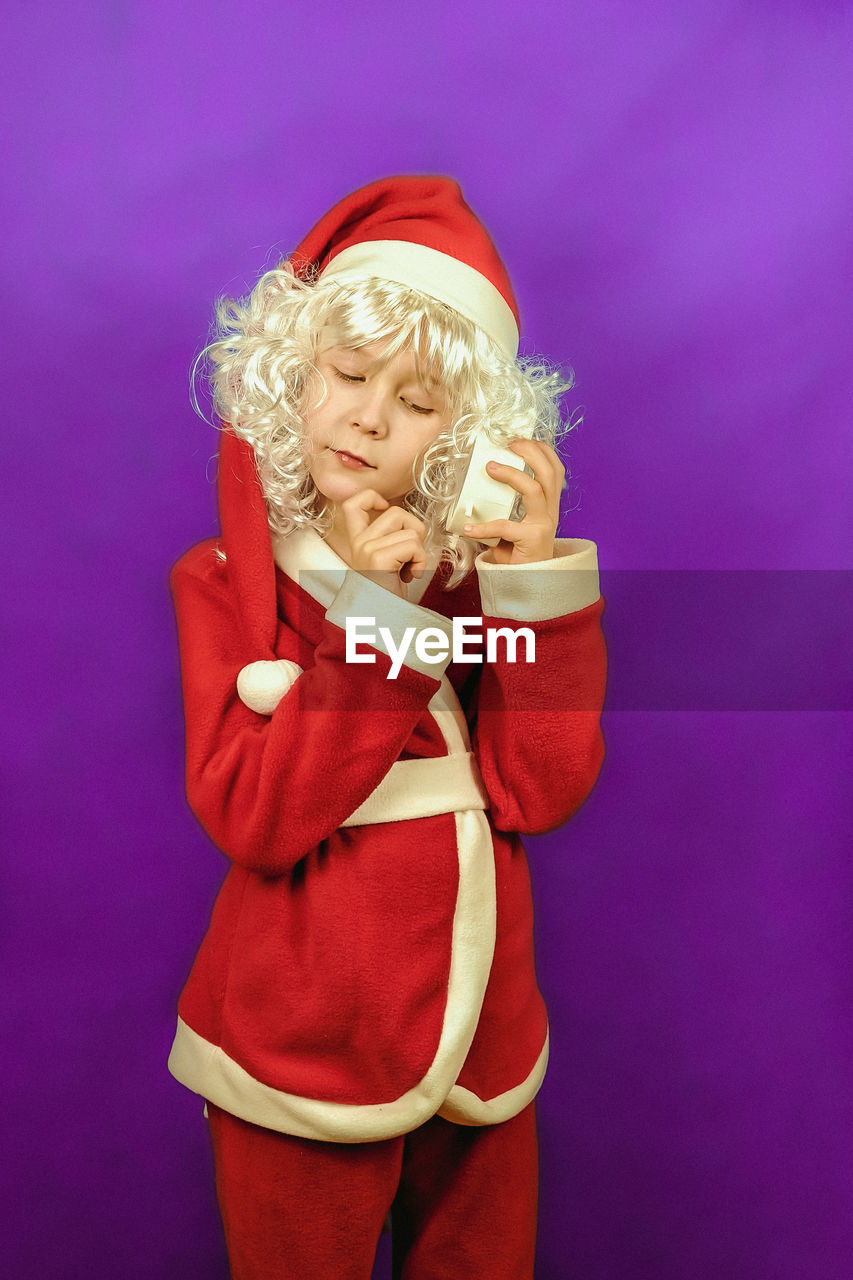 colored background, studio shot, blond hair, one person, indoors, childhood, toy, pink, child, women, clothing, costume, portrait, standing, three quarter length, adult, female, santa claus, red, figurine, waist up, person, human face, purple background, front view, cartoon
