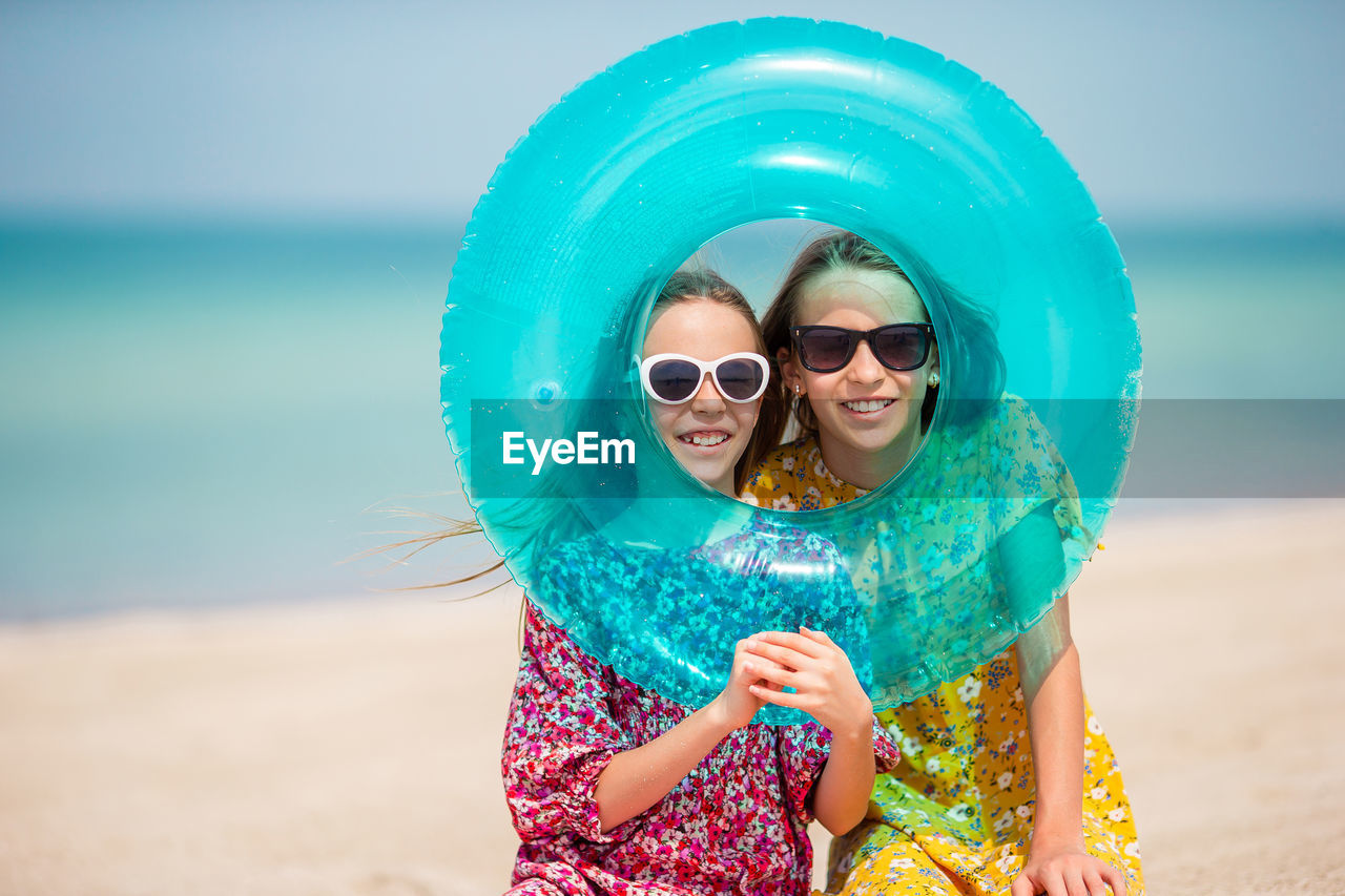 Portrait of smiling sisters wearing sunglasses seen through inflatable ring at beach