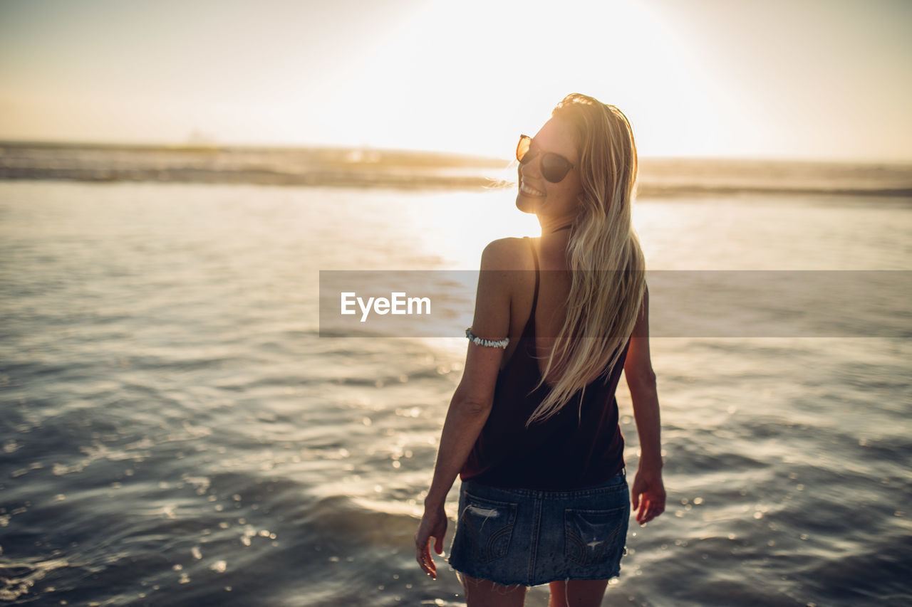 WOMAN STANDING AT BEACH AGAINST SKY