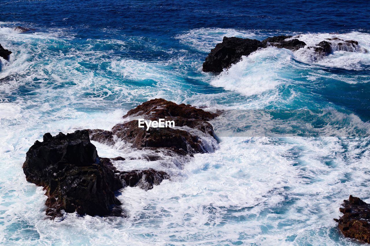 High angle view of waves splashing and crashing  on and over rocks white water surf 