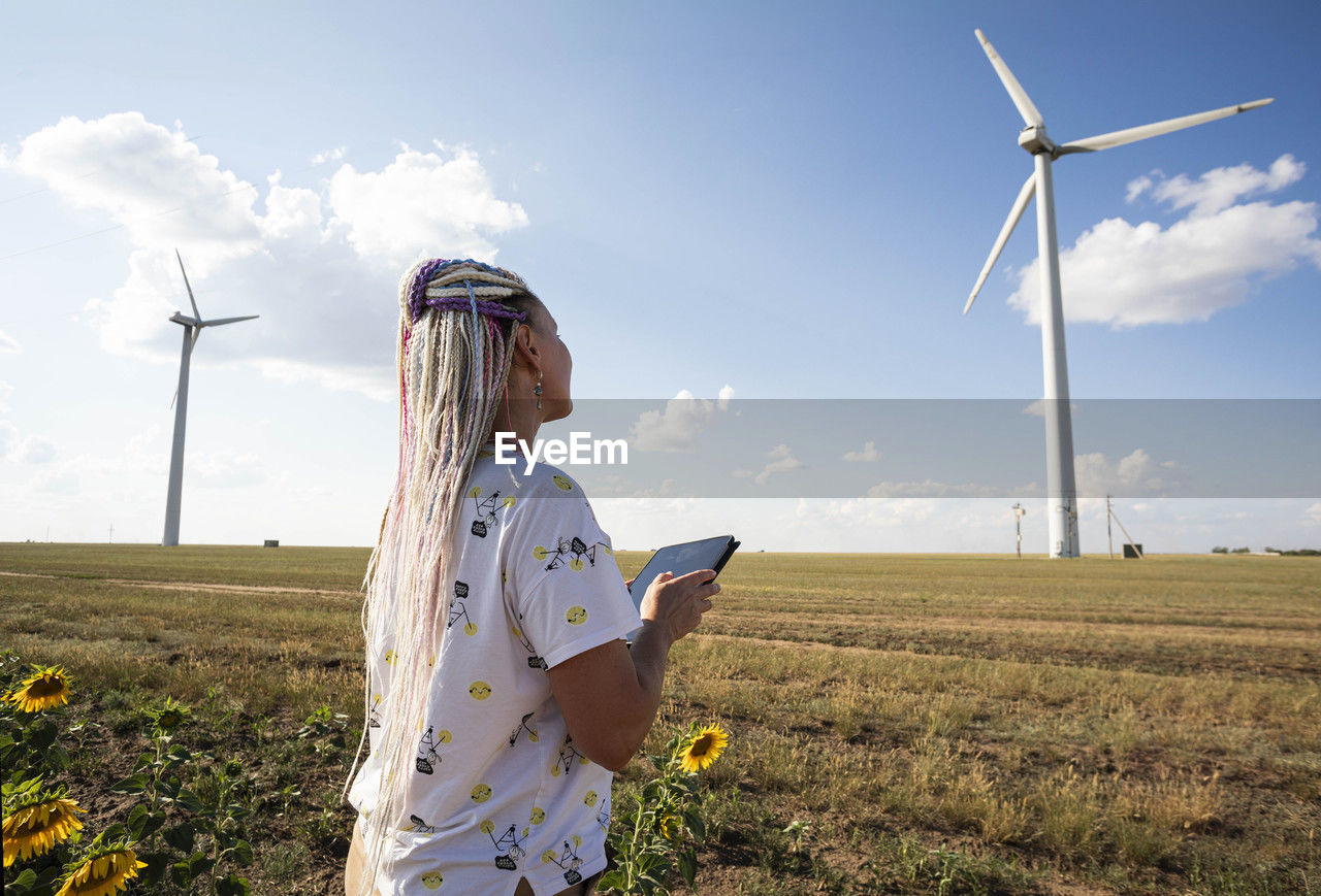 Young woman with tablet in field sunflowers, wind turbines for green energy production, eco-energy