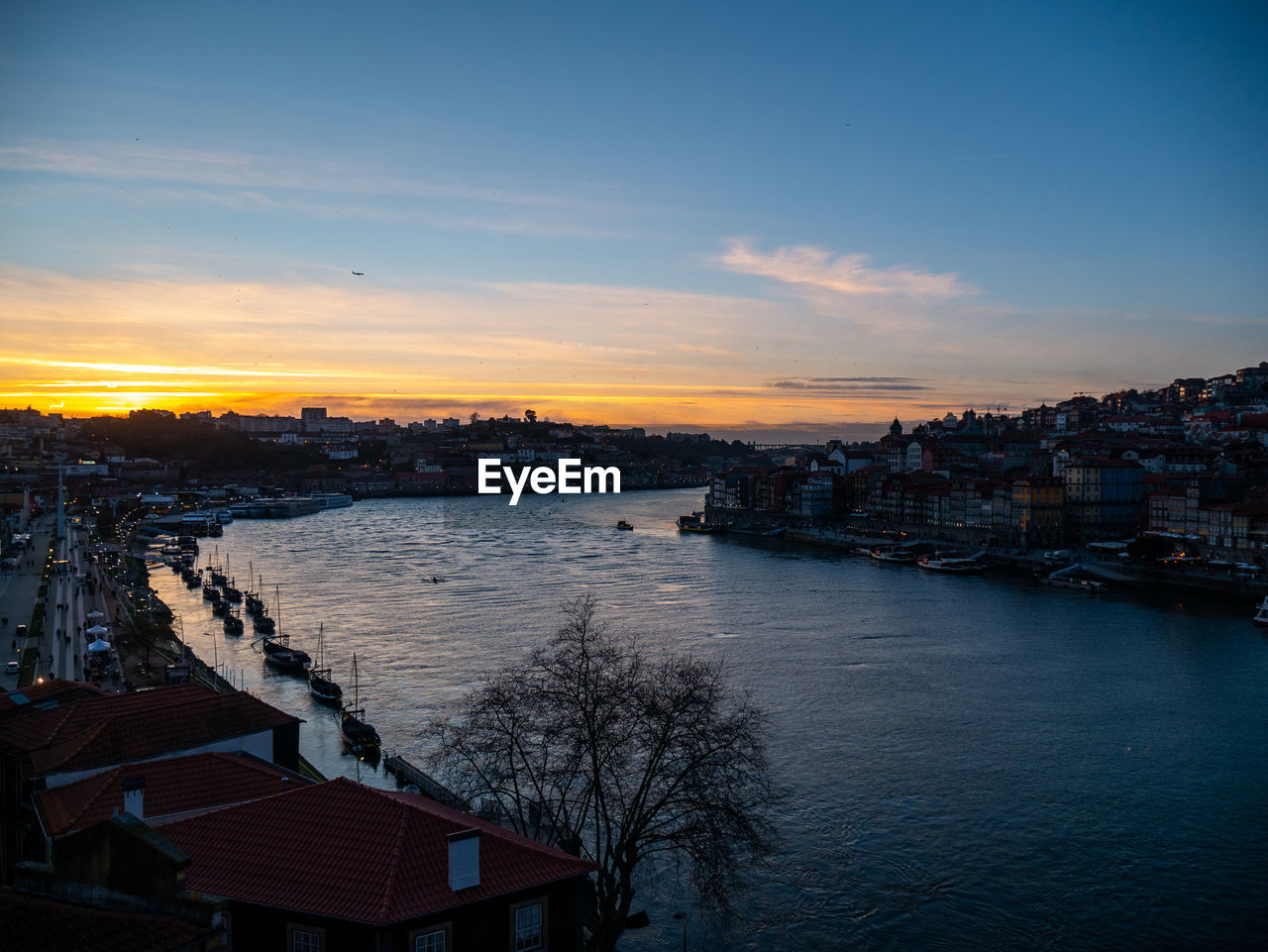 HIGH ANGLE VIEW OF RIVER AND BUILDINGS AGAINST SKY DURING SUNSET