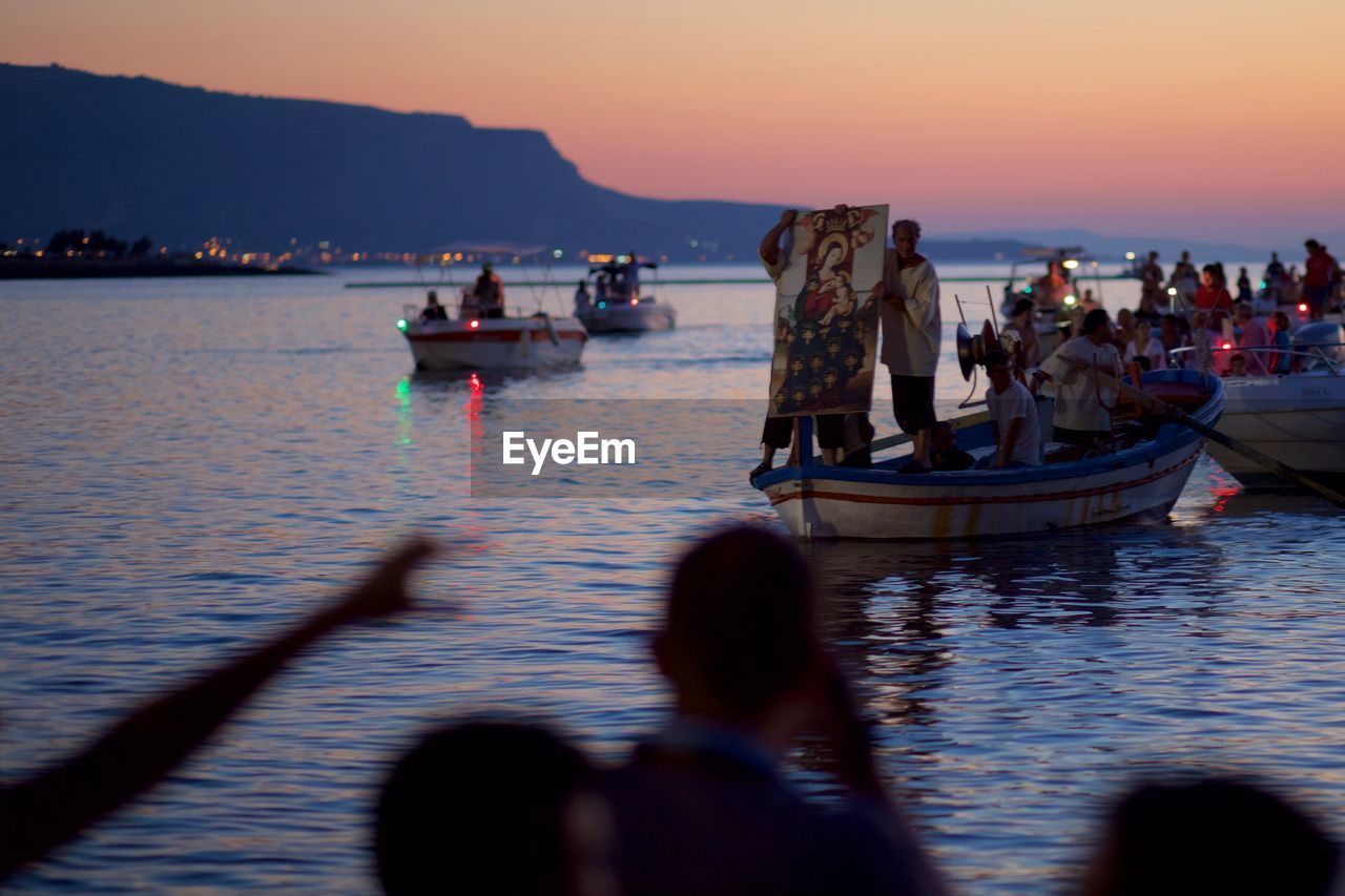 People on boats in sea against sky during sunset